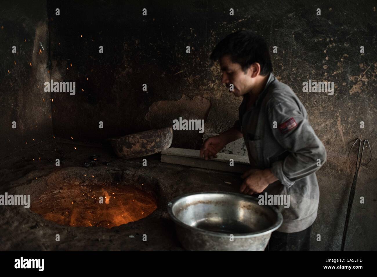 Kashgar, China, Región Autónoma de Xinjiang Uygur. El 2 de julio, 2016. Un panadero poner algo de leña en un horno de ladrillo para hornear Nang, una especie de panqueque crujiente, alimento básico de la población de Kashgar, en Kashgar, en el noroeste de China la Región Autónoma de Xinjiang Uygur, 2 de julio de 2016. Panaderos pasó más de 16 horas haciendo unas cuatro o cinco mil nangs para satisfacer las necesidades como romper el ayuno se está acercando. © Bu Duomen/Xinhua/Alamy Live News Foto de stock