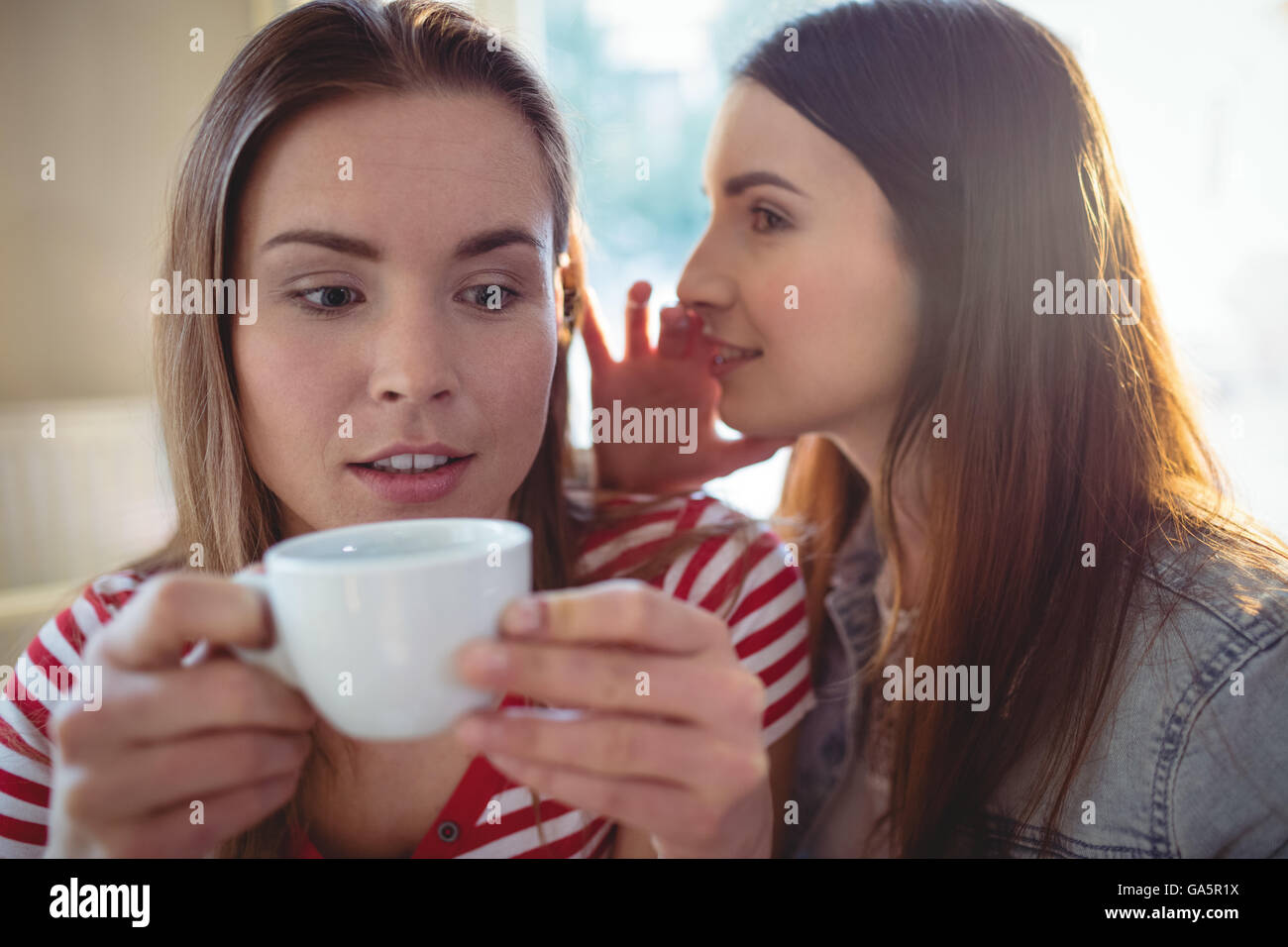 Mujer susurrando a un amigo en el café Foto de stock