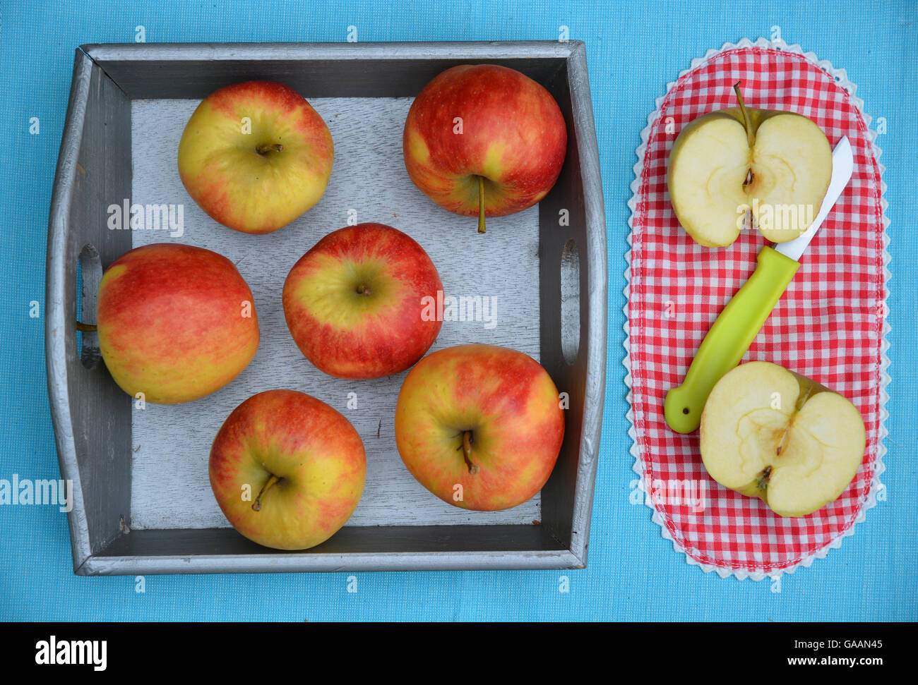 Brillantes cortadas frescas manzanas en una canasta de madera con un cuchillo y una tela a cuadros rojo y blanco Foto de stock