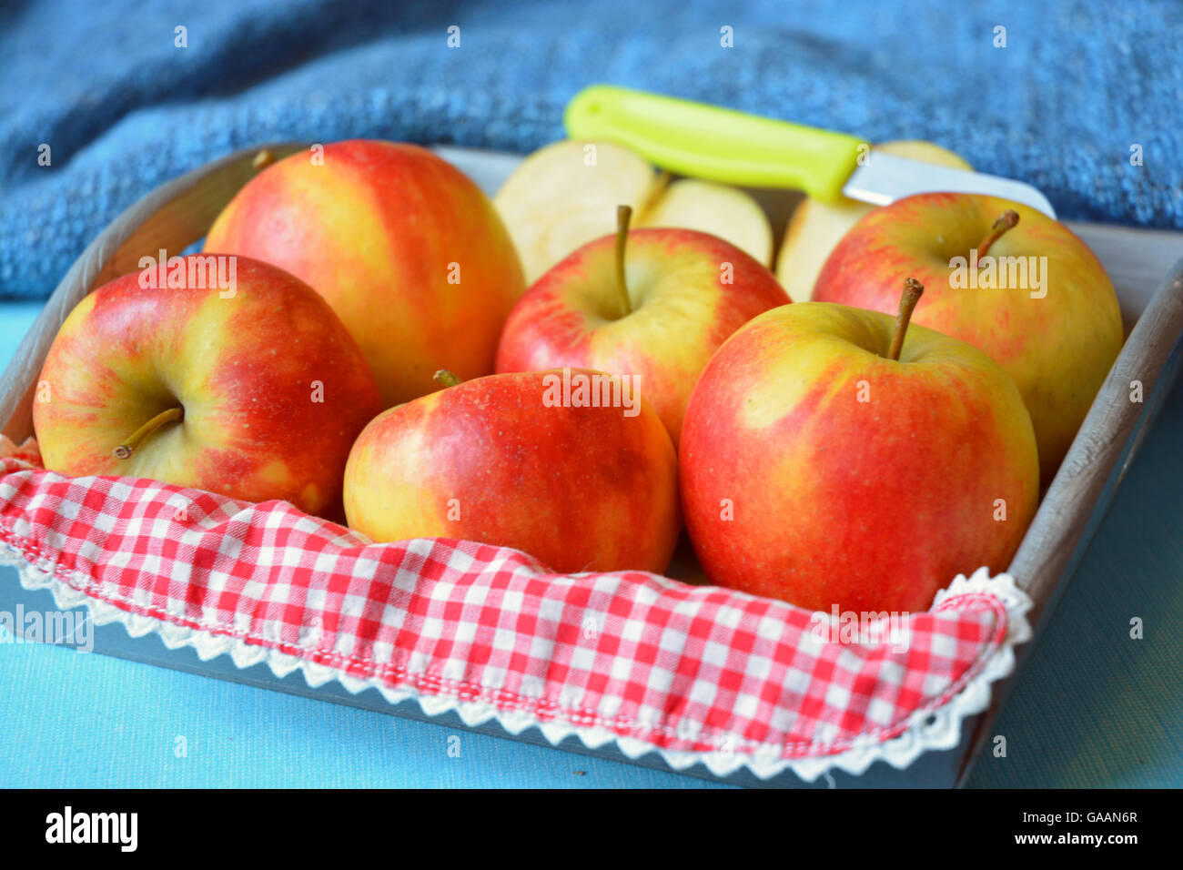 Brillantes cortadas frescas manzanas en una canasta de madera con un cuchillo y una tela a cuadros rojo y blanco Foto de stock