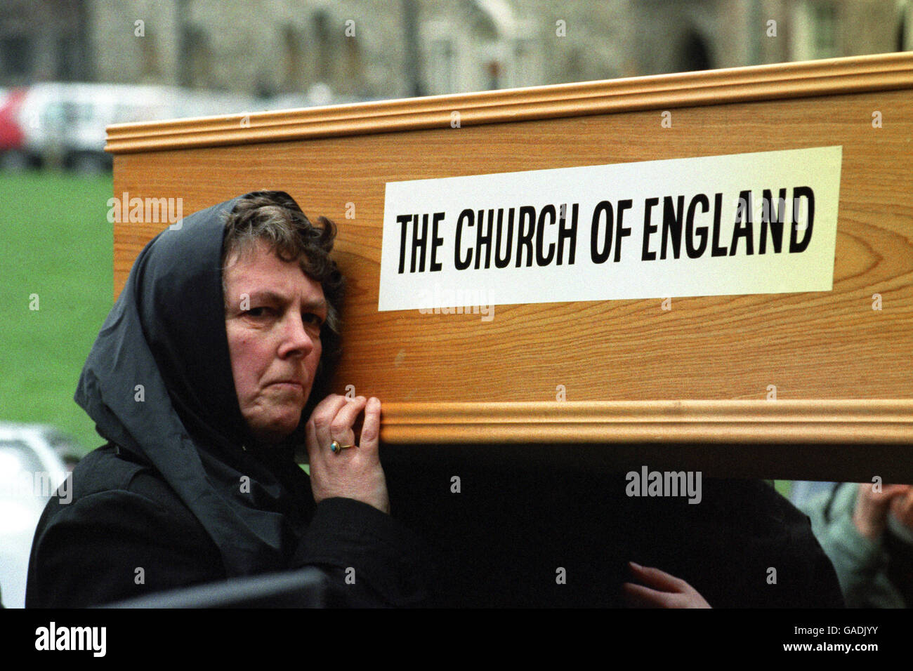 Una mujer ayuda a llevar un ataúd para simbolizar los 'últimos ritos de la Iglesia de Inglaterra'. Ecclesia dirigida por el Padre Francis Bown, organizó la protesta el día de la reunión general del Sínodo en Westminster. Foto de stock