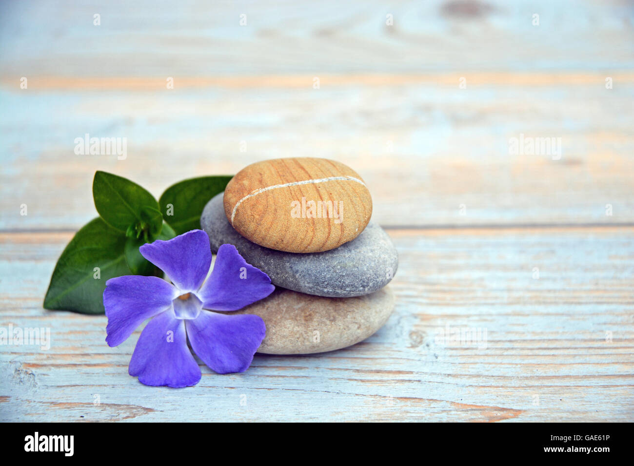 Tres Piedras cairn zen sobre un fondo de madera con una margarita y periwinkle Foto de stock