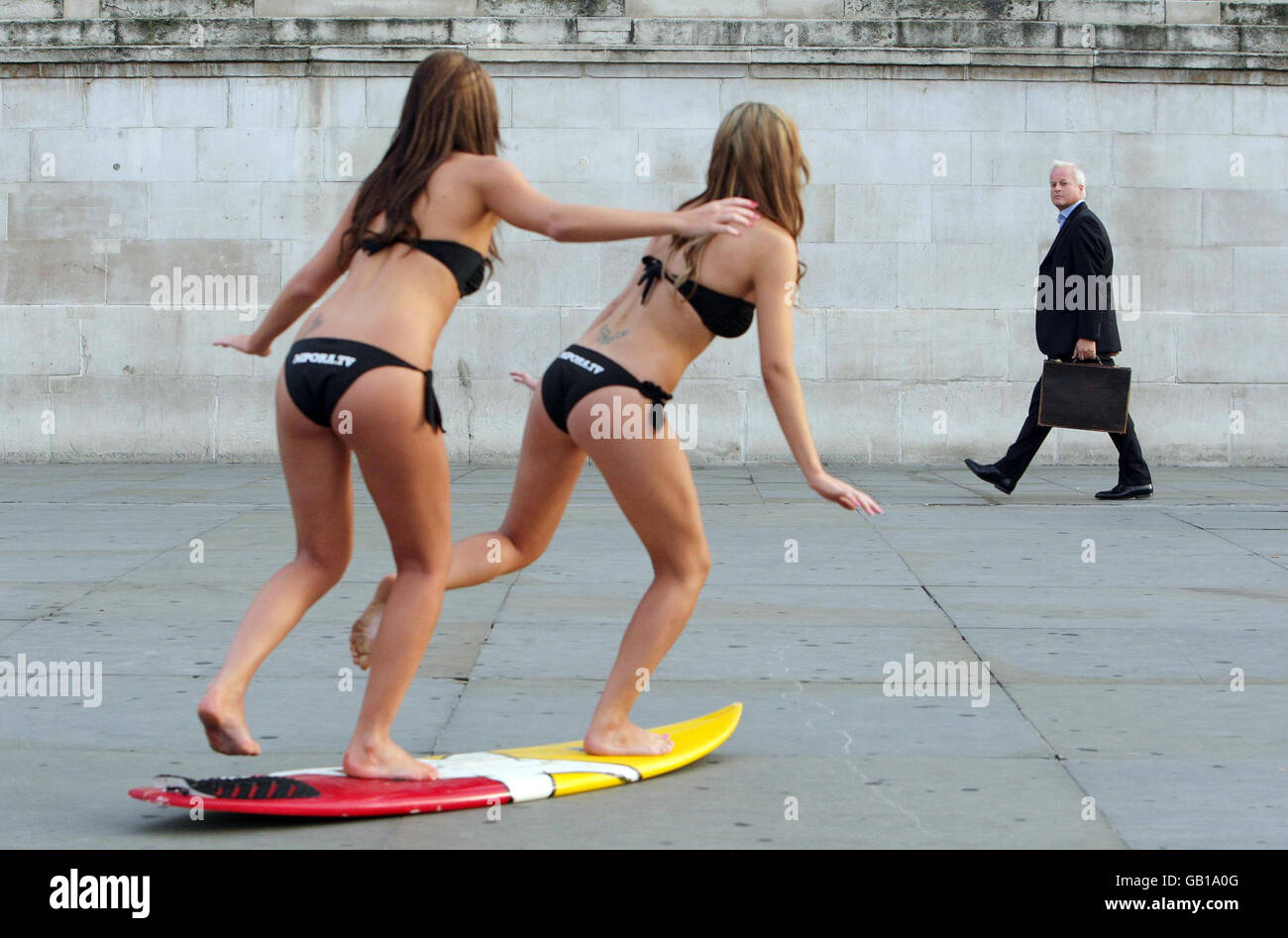 Los modelos Kristina Andriotis (izquierda) y Natasha Andriotis atraen la atención de un transeúnte al lanzamiento del canal de deportes extremos de Internet MPORA.TV, en Trafalgar Square, Londres. Foto de stock