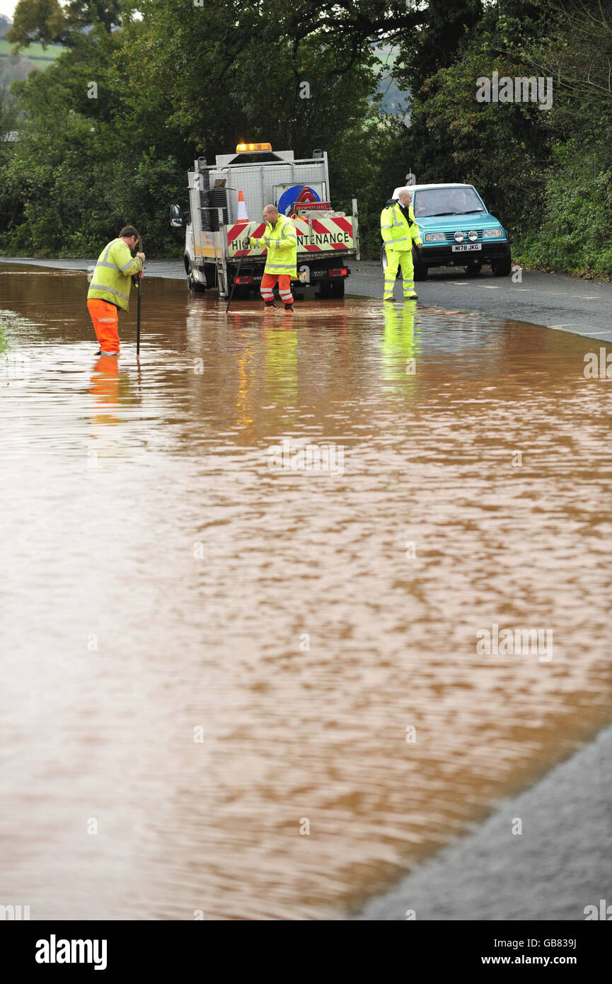 Los trabajadores de mantenimiento de carreteras trabajan para limpiar el drenaje en la B3181 en Westcott, Devon después de que una fuerte lluvia nocturna cerró la carretera y causó problemas de viaje en la región. Foto de stock