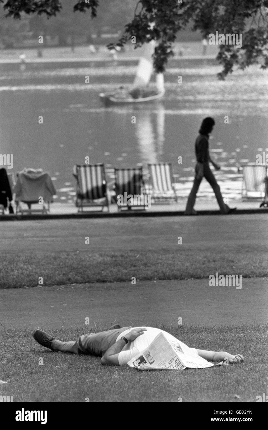 Un hombre tomando el sol bajo un periódico cerca del Serpentine en Hyde Park, Londres. Foto de stock