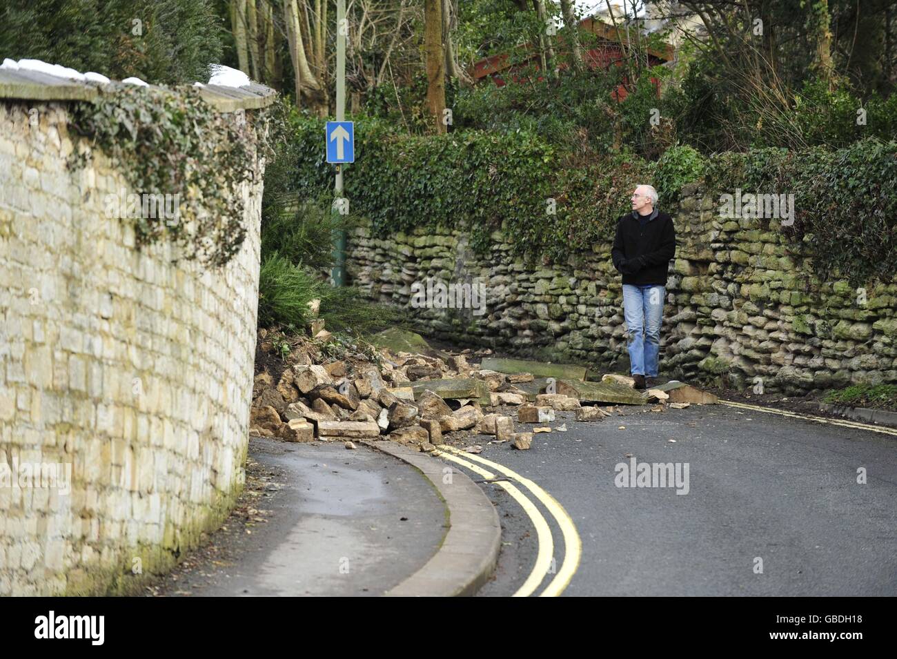 Mick Palmer se encuentra junto a su enorme pared de piedra que se derrumbó y bloquea Woolley Street en Bradford on Avon, después de la lluvia torrencial y la nieve en la ciudad. Foto de stock