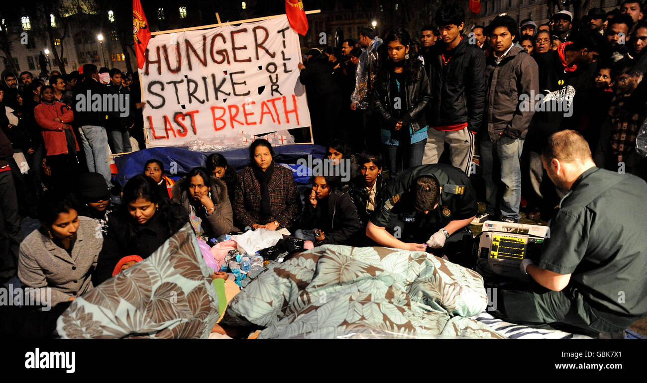La gente vigila mientras los médicos comprueban a Prarameswaran Subramaniam, de 28 años, y a Sivatharsan Sivakumaraval, de 21 años, estudiantes de Mitcham, en el sur de Londres, que están en huelga de hambre en la plaza del Parlamento de Londres, donde una protesta de unos 500 tamiles ha entrado su quinto día. Foto de stock