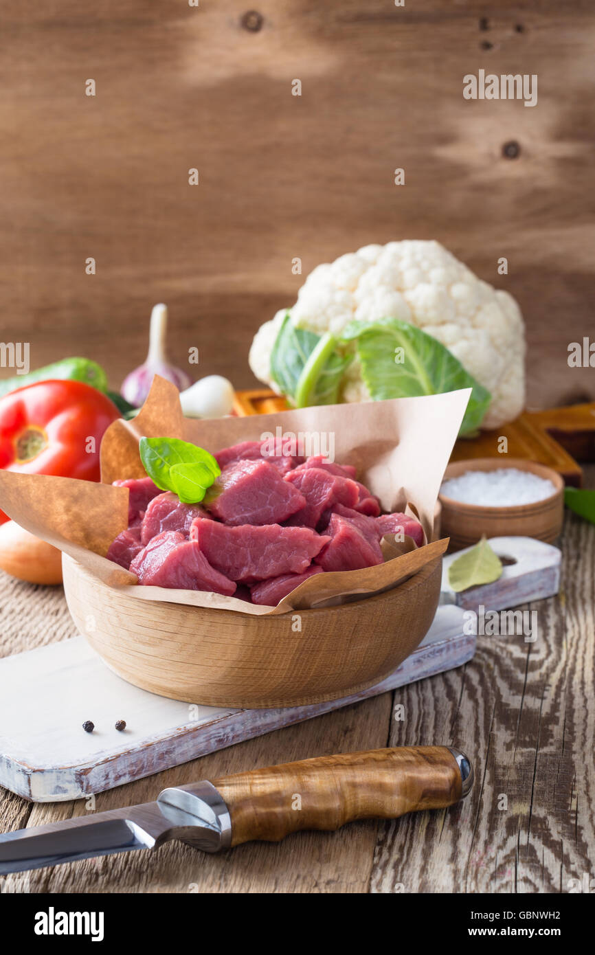 Ternera cruda cortada en trozos con verduras y otros ingredientes listos para cocinar en madera rústica mesa, concepto de cocina ecológica Foto de stock
