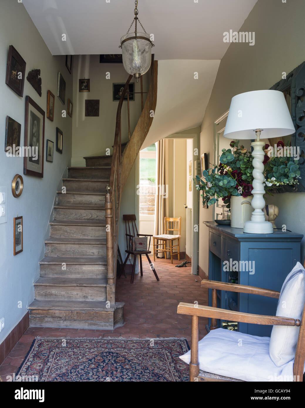 Hall de entrada con baldosas de terracota, escalera de madera y alfombras orientales Foto de stock