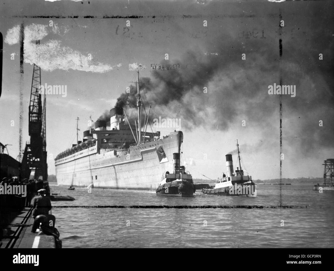 Dos pequeños y robustos remolcadores escoltan a la poderosa 'Reina María' mientras atraca en Southampton después de otro viaje por el Atlántico. Un estudio sorprendente del segundo soporte más grande del mundo. Mayo de 1st 1946 Foto de stock