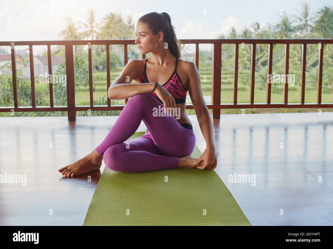 Foto de joven mujer caucásica sentado en la estera del yoga y apartar la mirada. Fitness femenino después de relajante sesión de ejercicio físico. Foto de stock