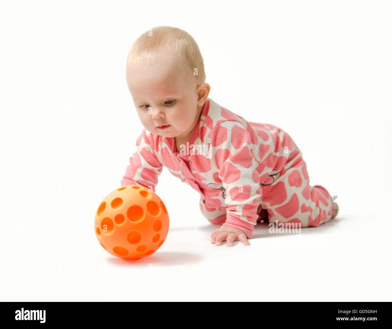 Niña vestidos de blanco y rosa pijama, calcetines rojos está jugando con su bola naranja mientras yace en un vientre Foto de stock