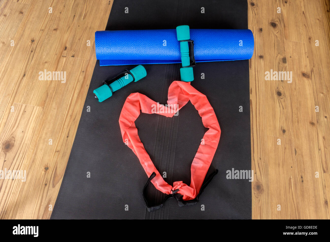 Colección de equipos para hacer ejercicio en la estera del yoga sobre un piso de madera con antecedentes de resistencia formando una banda en forma de corazón Foto de stock