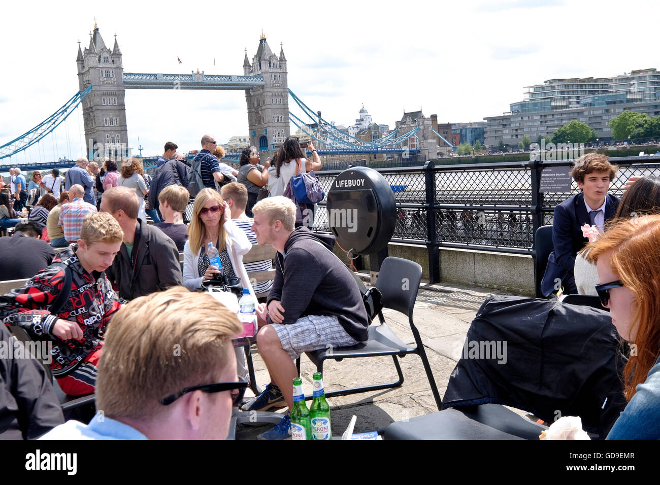 Los turistas tienen el almuerzo en un restaurante al aire libre en el Victoria Embankment a lo largo de río Támesis con el Tower Bridge de Londres, hitos en el fondo. Foto de stock