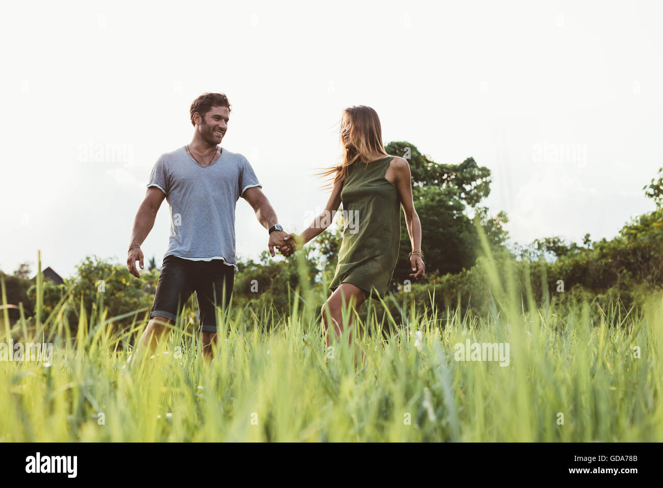 Foto de joven pareja caminando en la pradera. El hombre y la mujer tomados de la mano y caminar juntos en el campo de hierba alta. Foto de stock