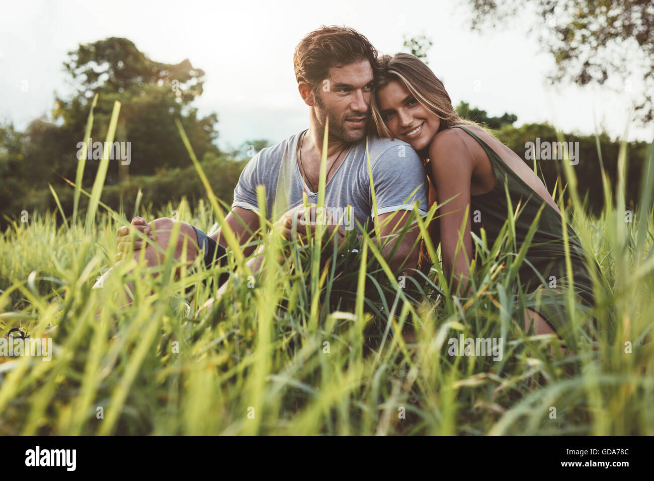 Disparo de afectuosa pareja joven disfrutando de un día al aire libre. Hombre y mujer sentada en campo de hierba en un día de verano. Foto de stock