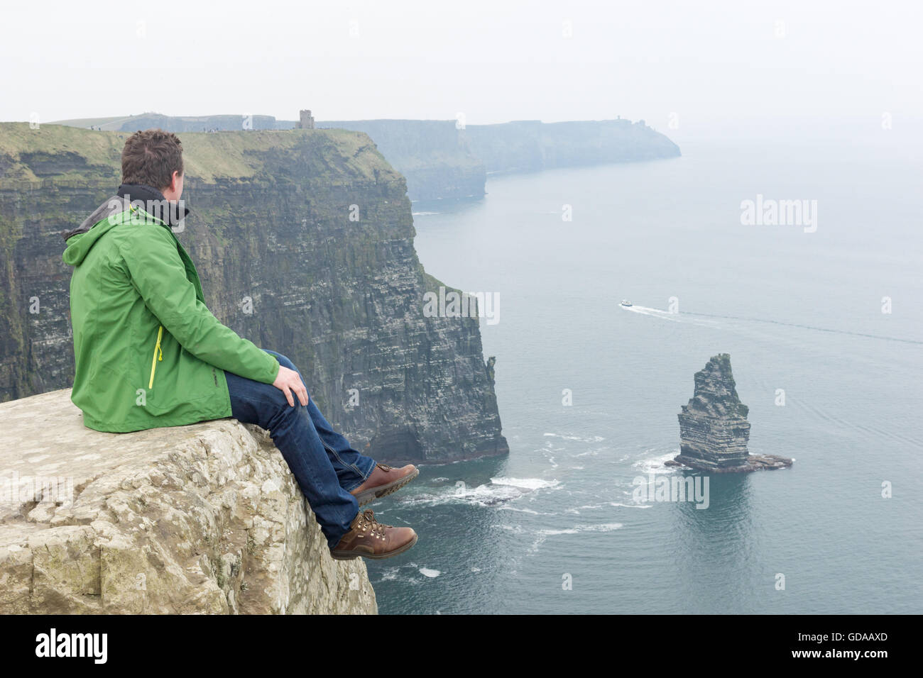 Irlanda, en el condado de Clare, acantilados de Moher, hombre sentado en lo alto de una roca Foto de stock