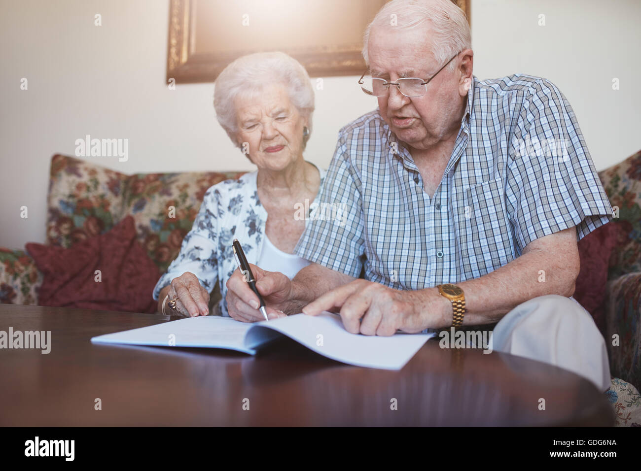 Filmación en interiores de la pareja de ancianos en casa firma papeleo juntos. Se retiró un hombre y una mujer sentados en el sofá y atravesando algunos Foto de stock