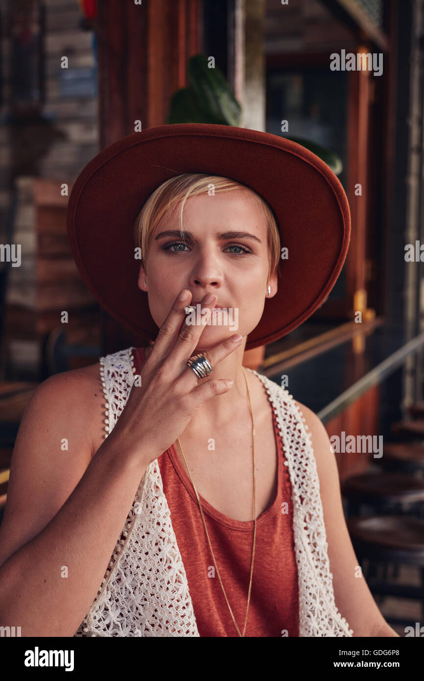 Retrato de mujer joven con sombrero de fumar un cigarrillo en una cafetería. Foto de stock