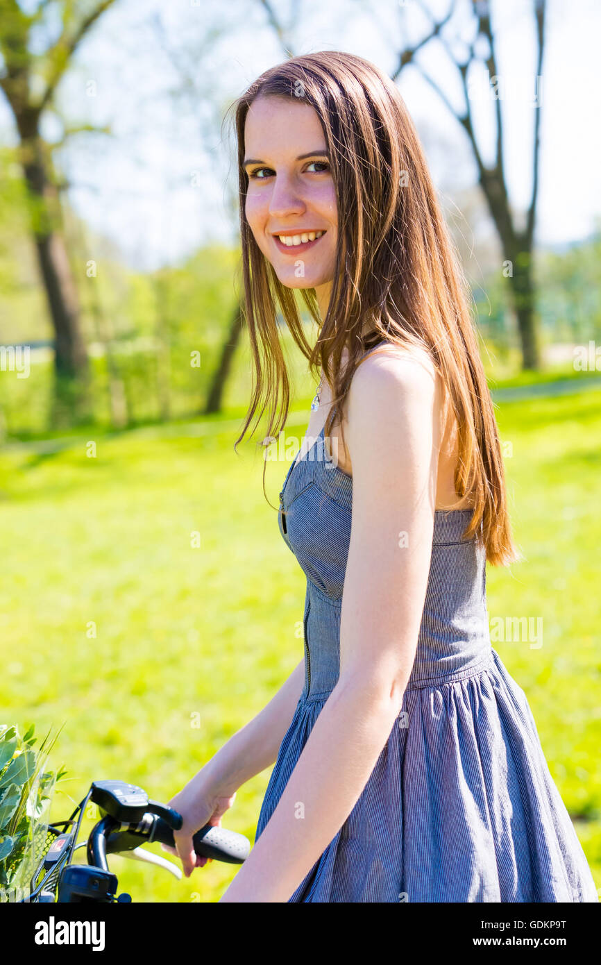 Mujer joven con pelo largo uso para viajar en bicicleta en la naturaleza, mirar a cámara y sonreír Foto de stock