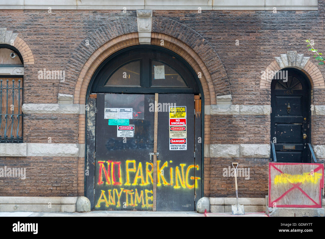La Ciudad de Nueva York fachada de ladrillo edificio en construcción con permisos, advertencias y el aparcamiento no siempre pintado con spray en las puertas. Foto de stock