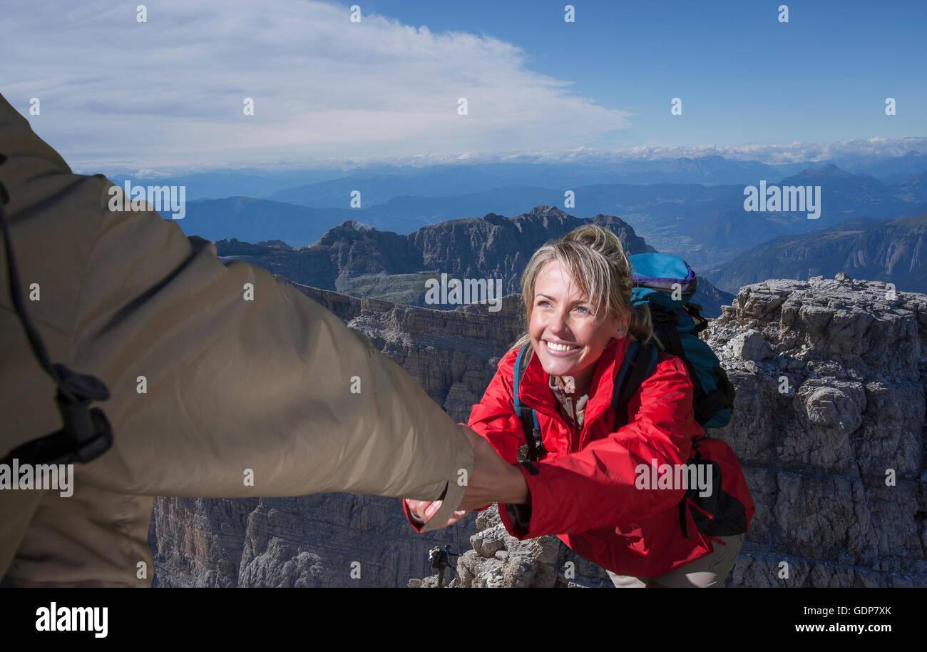 Un escalador masculino ayudando a su pareja femenina para llegar a la cima de una montaña, Dolomitas, Italia Foto de stock