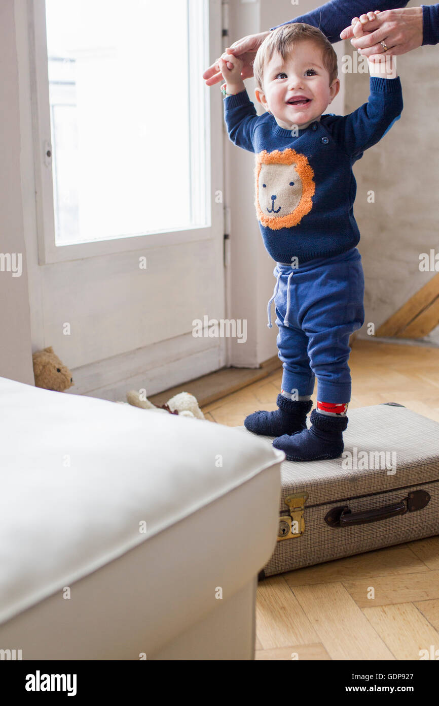 Baby Boy sosteniendo las madres manos y pararse en la maleta Foto de stock