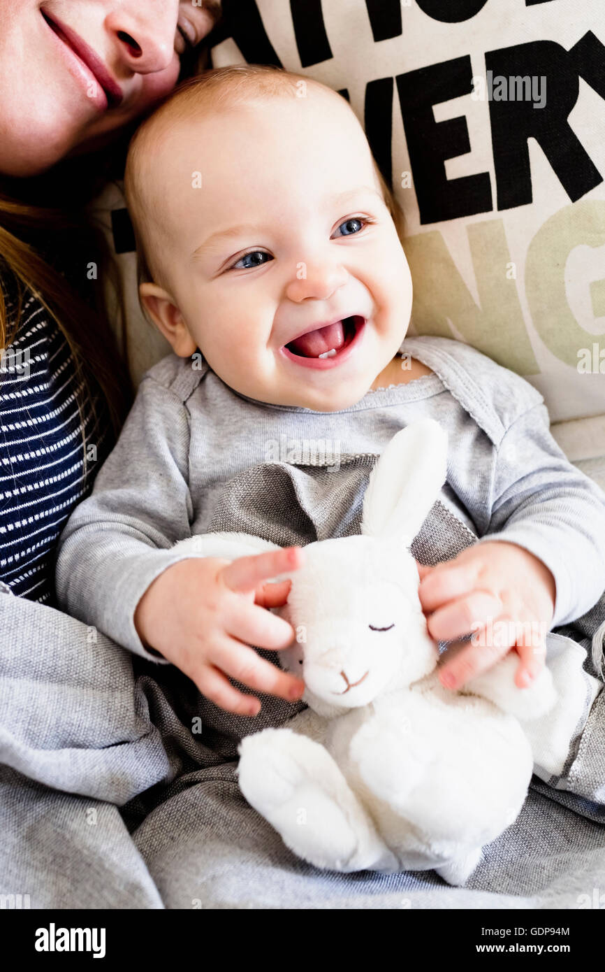 Niña y madre recostada en el sofá con conejo de juguete Foto de stock