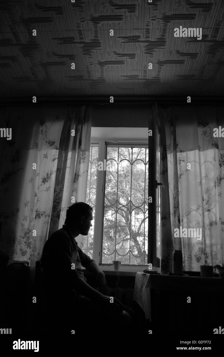 Silueta de un hombre sentado en la habitación y mirando a través de la ventana Foto de stock