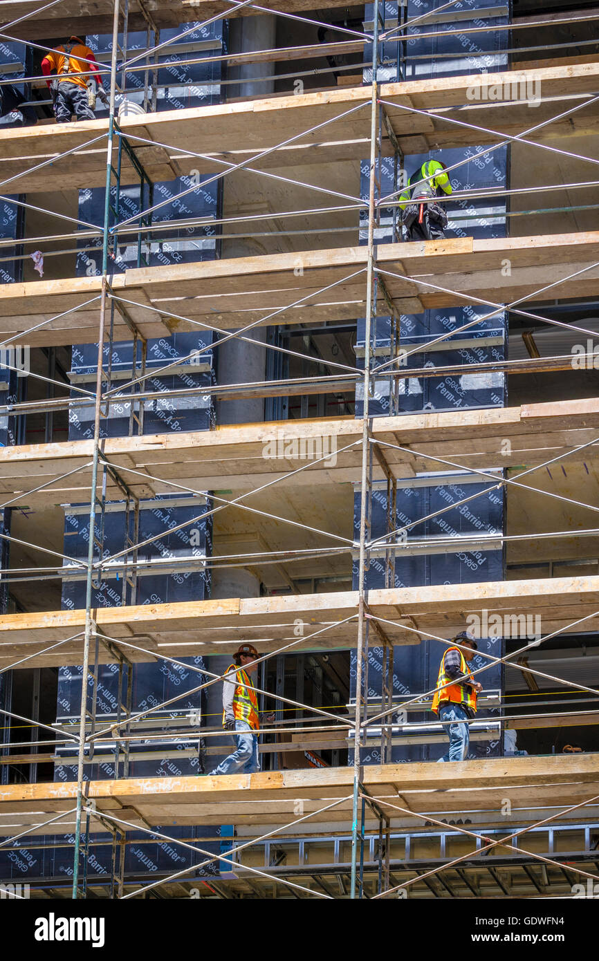 Los hombres que trabajan en diferentes niveles de andamios en tall office en construcción Foto de stock