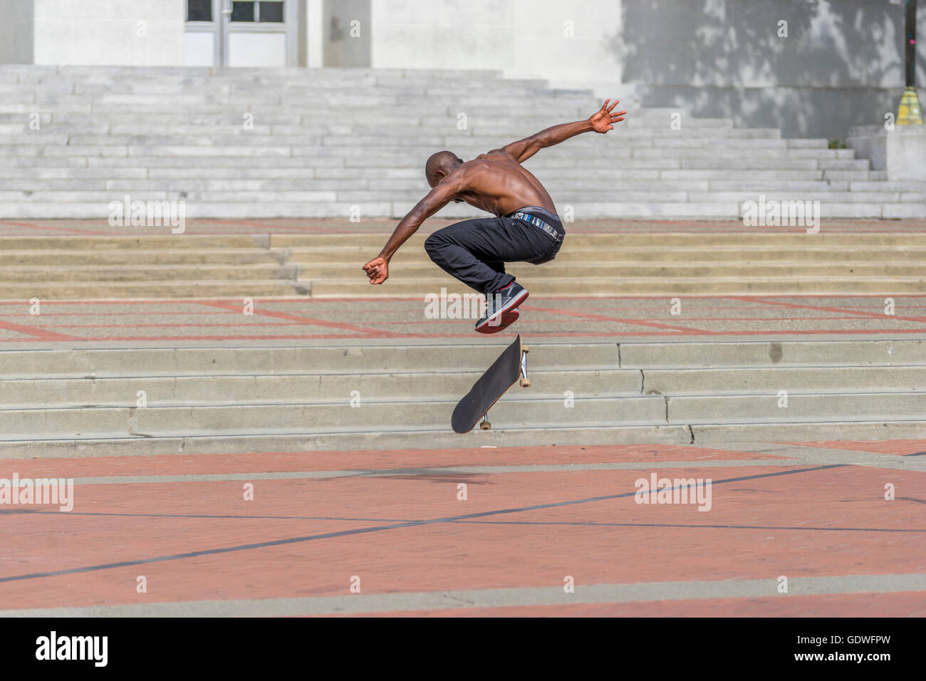 Hombre saltar alto en el aire mientras practica su kickflip truco en su monopatín Foto de stock