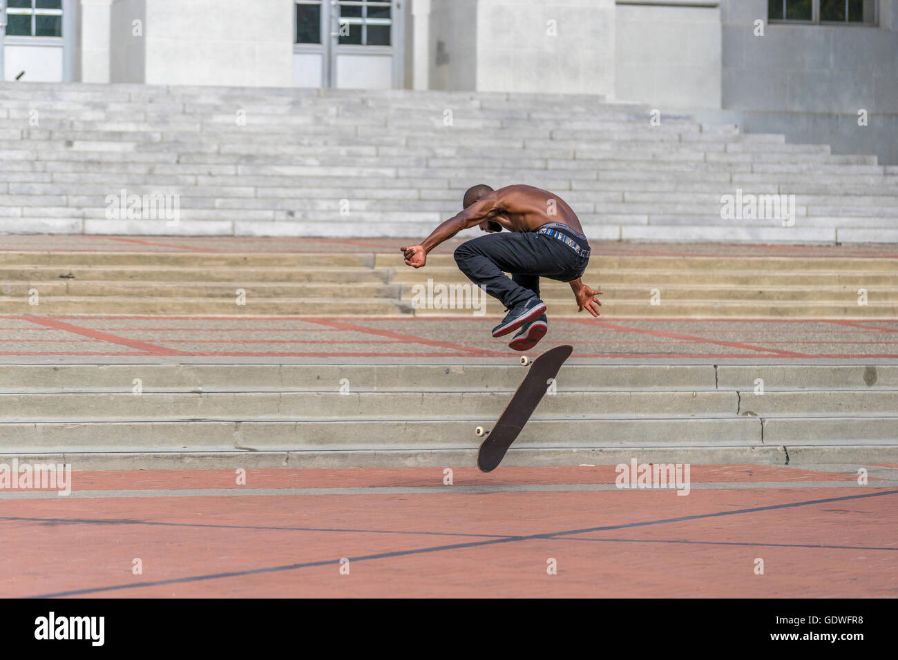 Hombre saltando en el aire mientras practica su kickflip truco en su monopatín Foto de stock