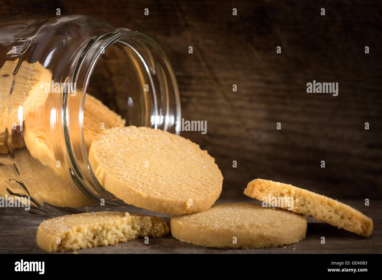 Galletas de mantequilla casera saliendo de un tarro de vidrio sobre una mesa de madera. Foto de stock