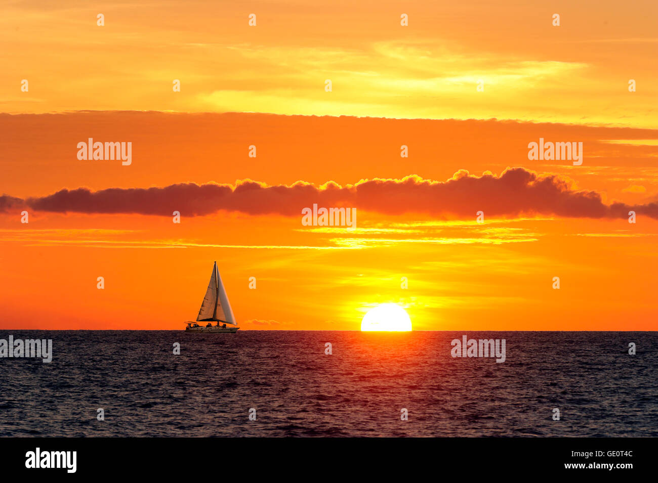 La vela Sunset es un velero que se mueve a lo largo del agua a medida que el sol va abajo en el horizonte del océano. Foto de stock
