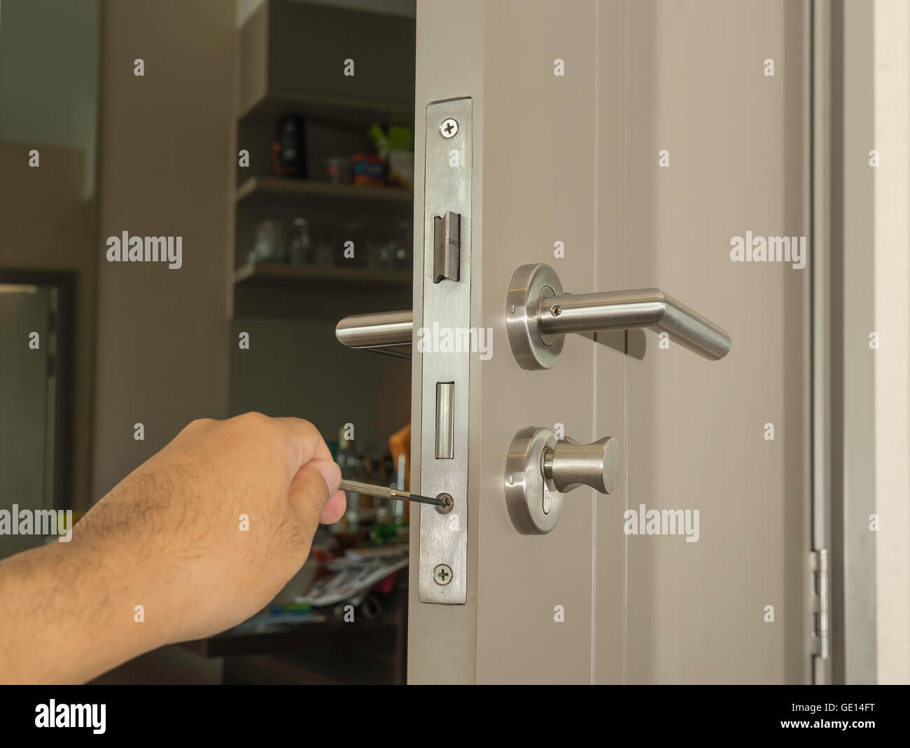Cerrajero intentan fijar la puerta en la habitación moderna con un destornillador y mano izquierda Foto de stock