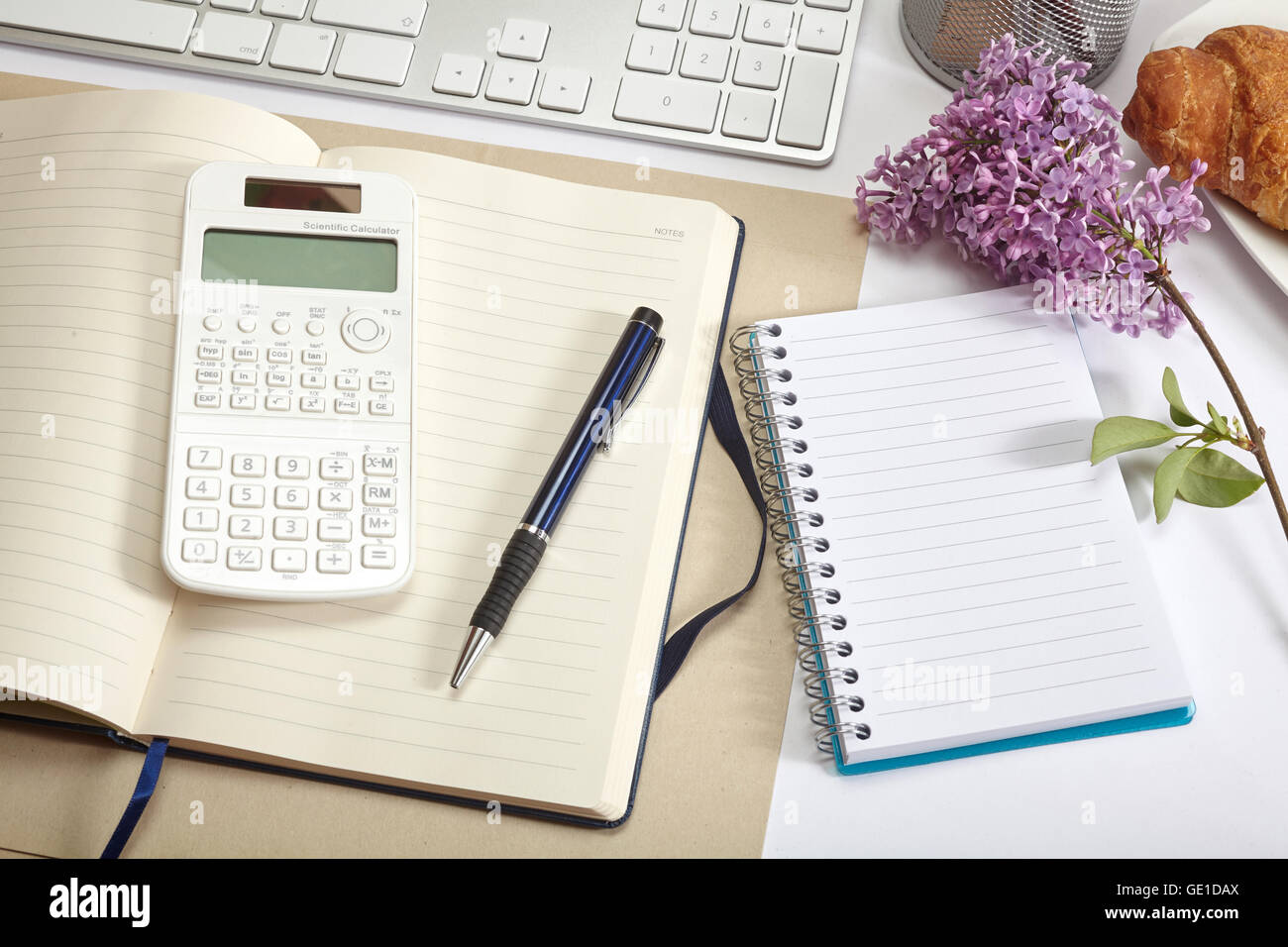 Vista superior de la oficina - croissant, teclado, calculadora, lápiz, flor y bloc de notas en el cuadro blanco Foto de stock