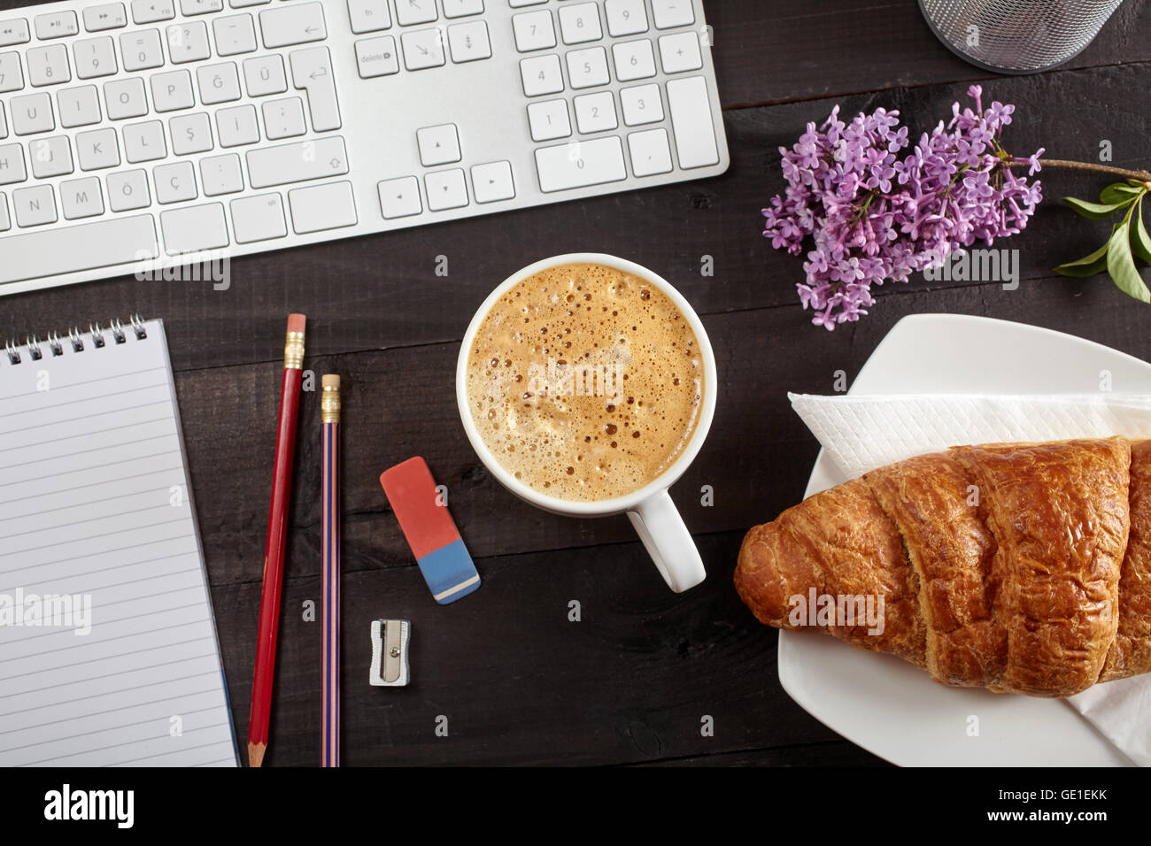 Vista superior de la oficina - café, teclado, lápiz, croissant, flor y bloc de notas en el cuadro negro Foto de stock