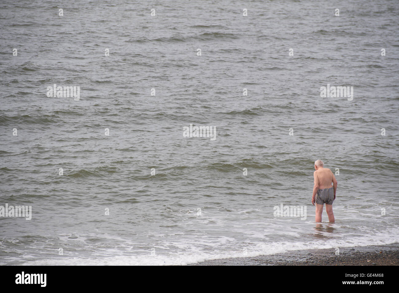 Mantenerse en forma en la vida posterior: senior masculino adulto viejo hombre de pie en el mar cerca para ir a nadar, UK Foto de stock