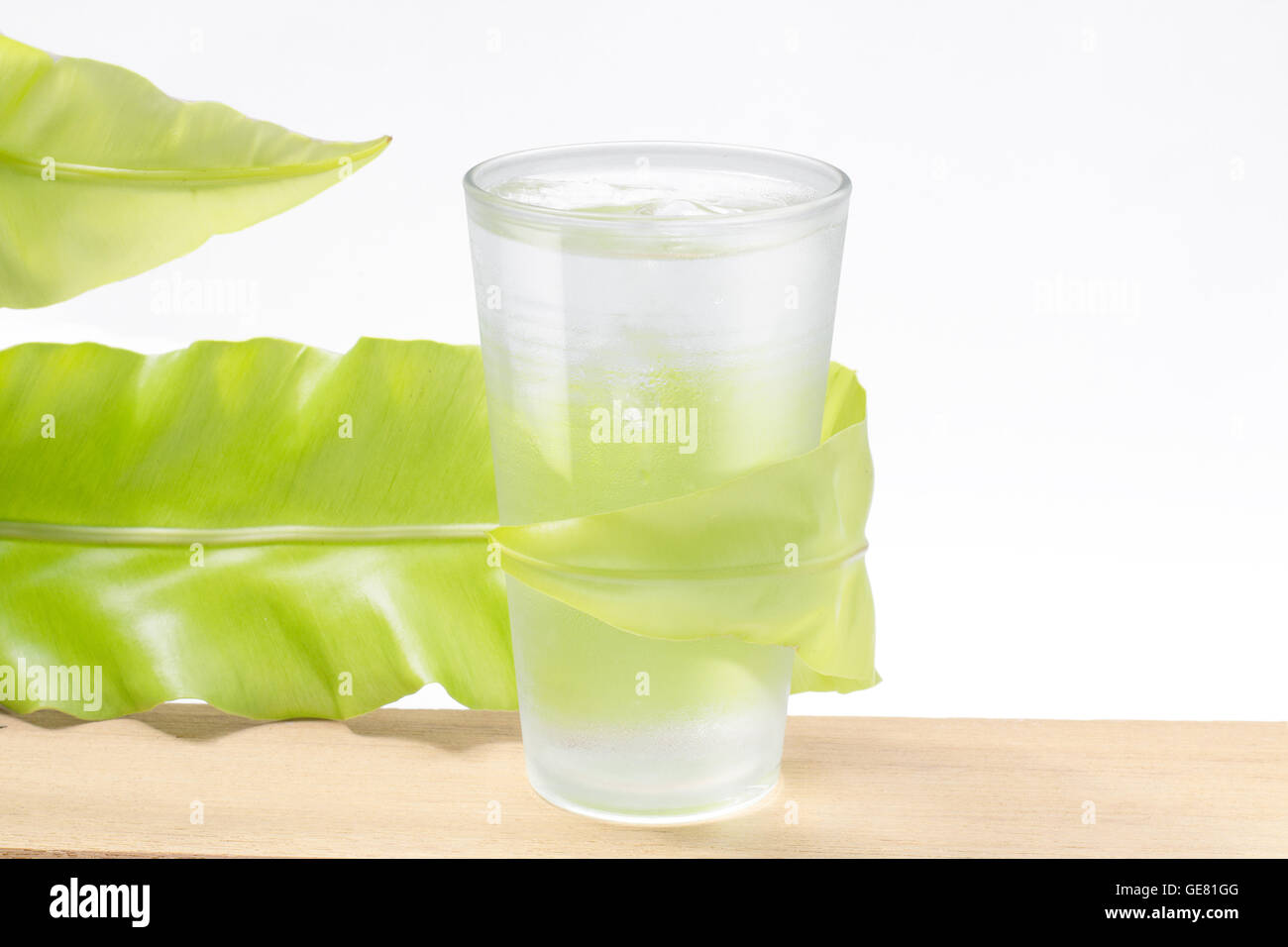Agua fresca de vidrio con hojas verdes sobre fondo blanco. Foto de stock