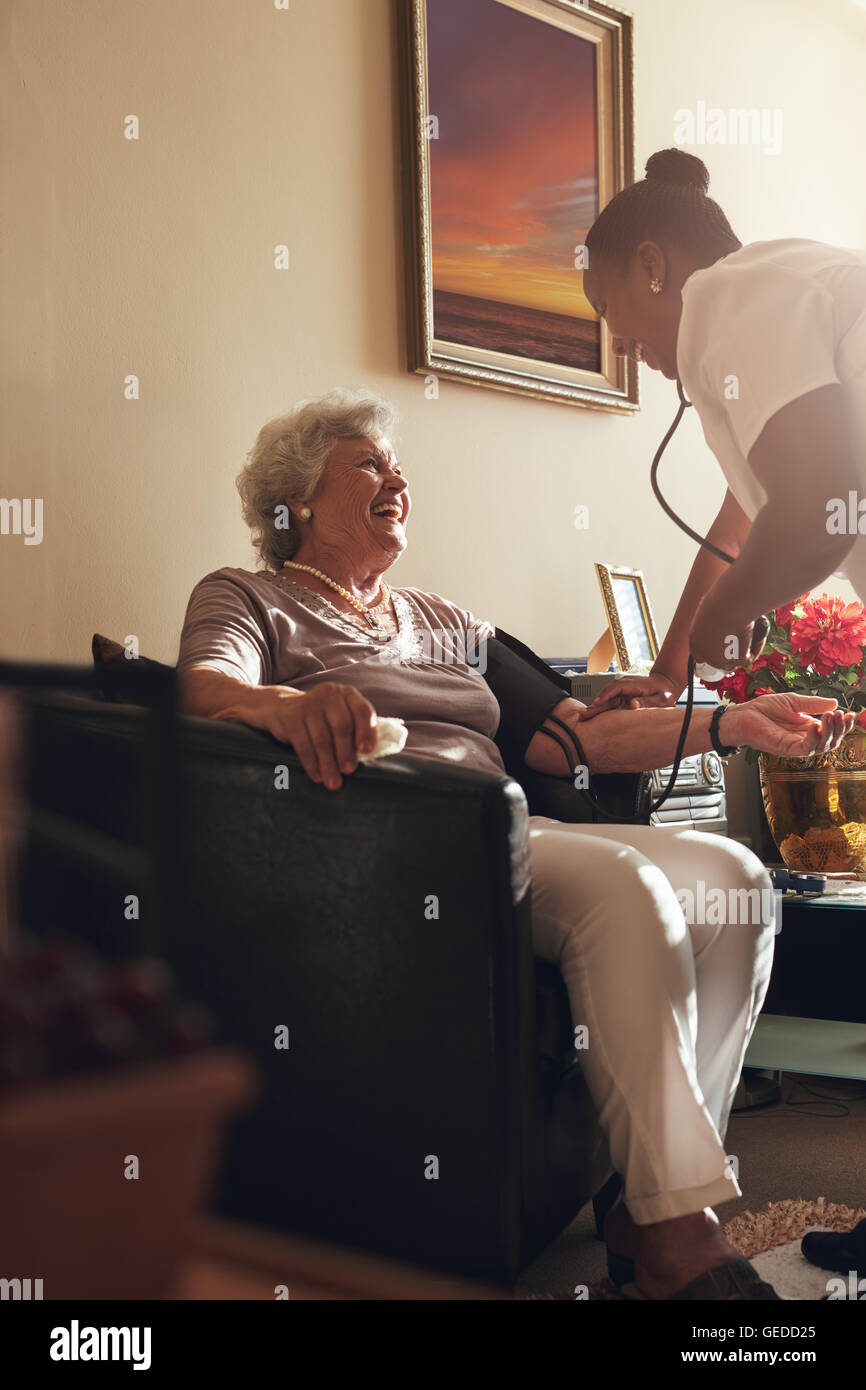 Casa cuidador, la medición de la presión sanguínea del paciente senior en casa. Trabajador sanitario femenino haciendo chequeo de rutina de un anciano p Foto de stock