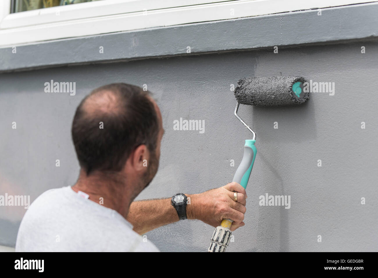 Un pintor y decorador de pintar la pared exterior de una casa con un rodillo. Foto de stock