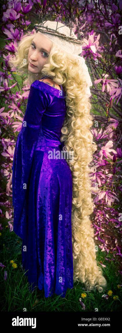 Mujer joven vestida como Rapunzel vestidos de terciopelo morado traje medieval con largo pelo rubio, rizado. Foto de stock