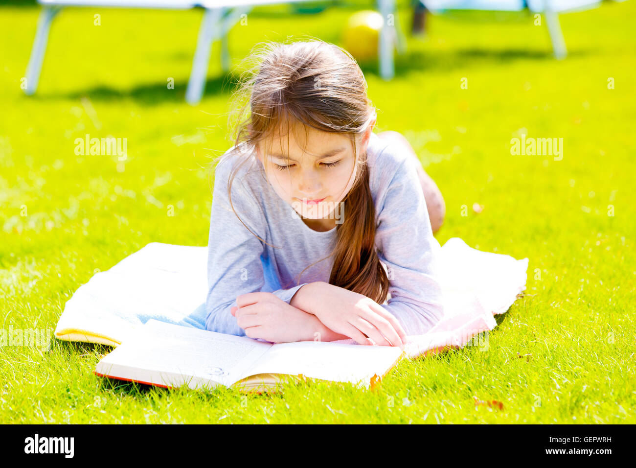 Los niños chica lea el libro sobre el pasto verde Foto de stock