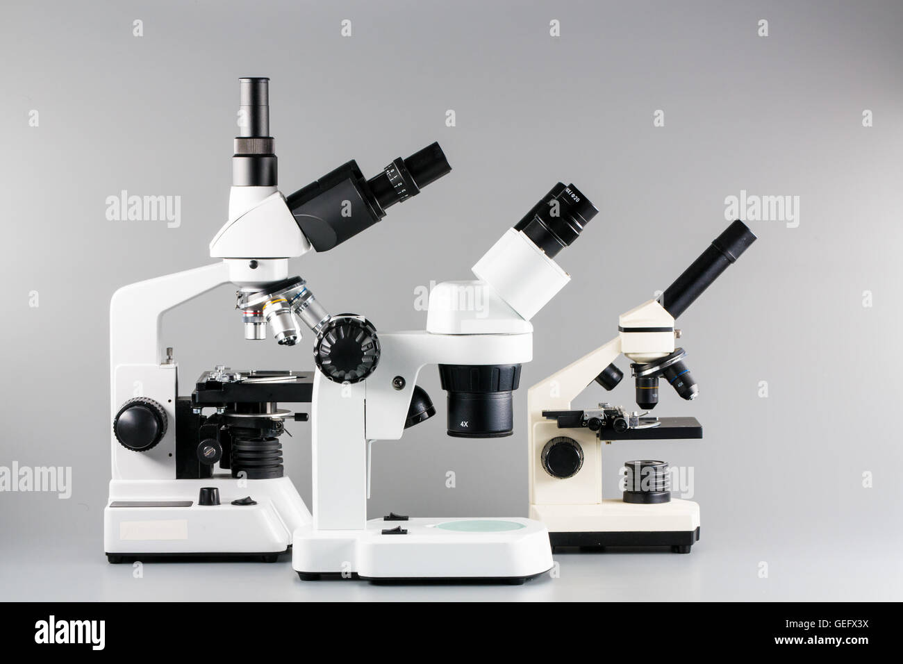 Monocular, binocular y trinocular microscopios sobre fondo gris Foto de stock