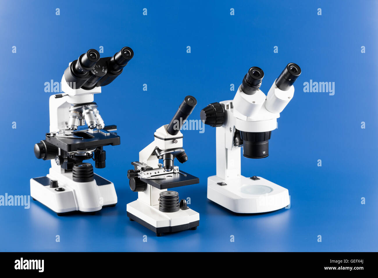 Monocular, binocular y trinocular microscopios sobre fondo azul. Foto de stock
