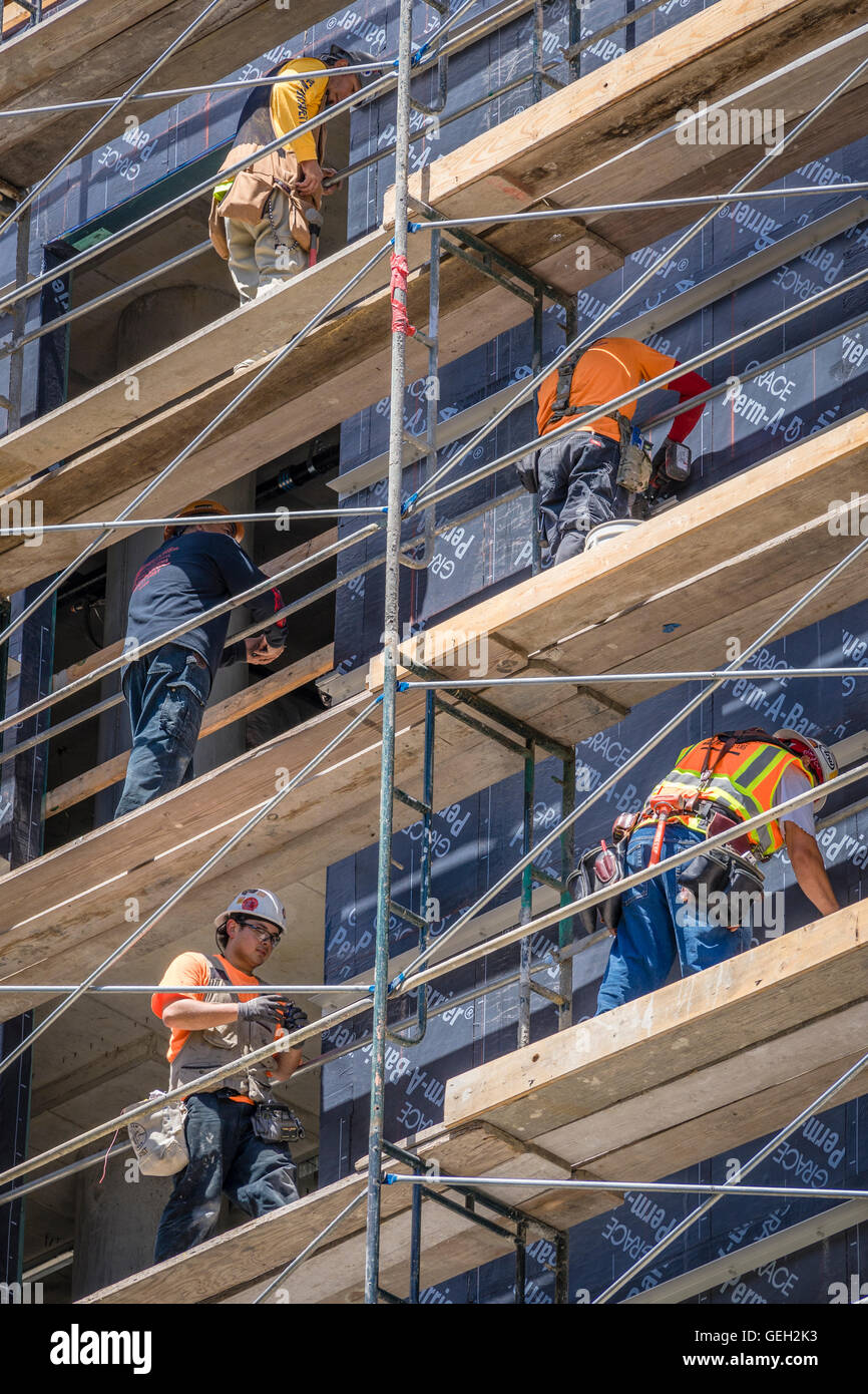 Cinco trabajadores de la construcción en diferentes niveles de andamios durante el desarrollo del edificio alto Foto de stock