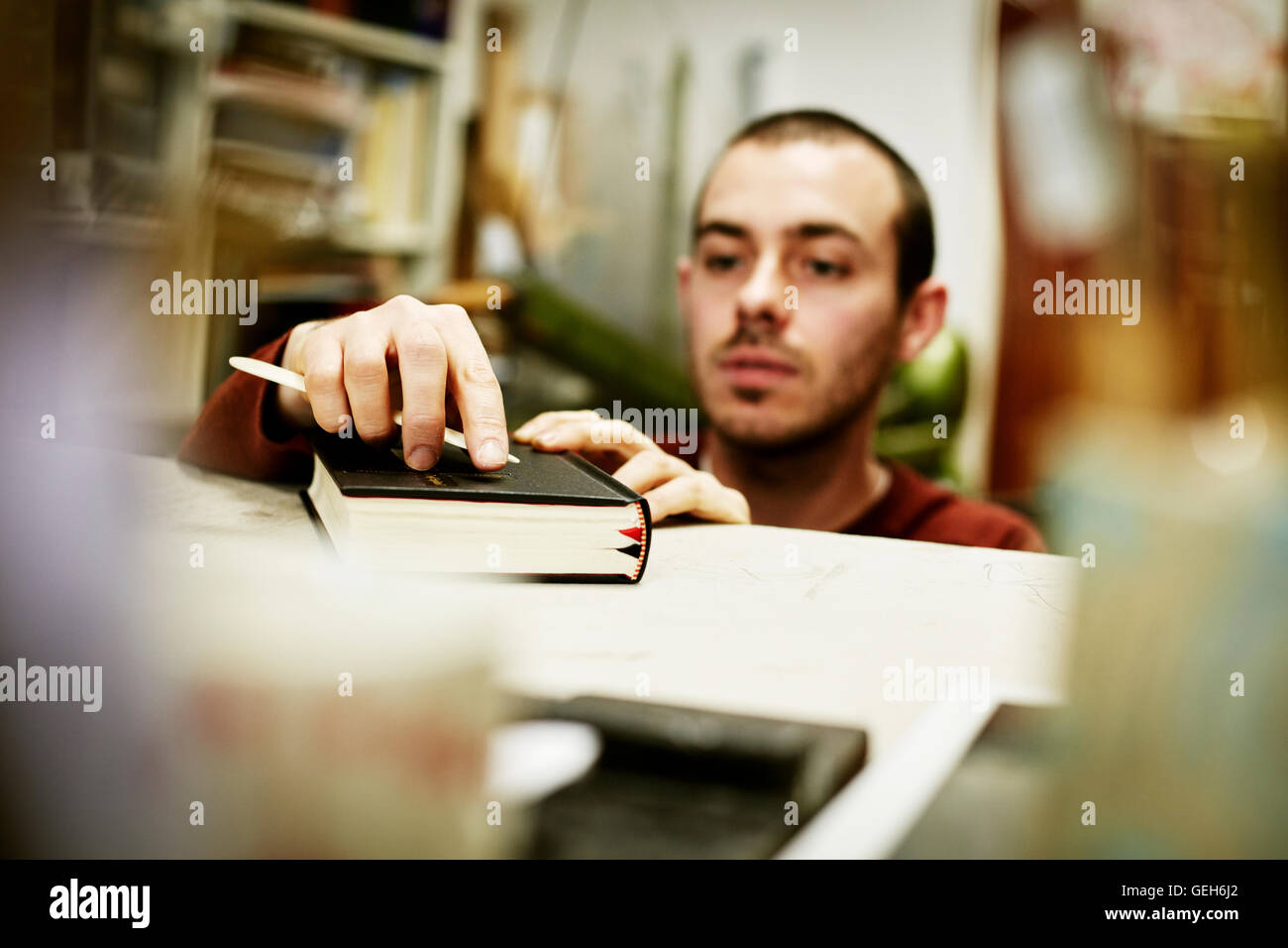 Un hombre usando una herramienta de mano sobre la cubierta de un libro. Foto de stock
