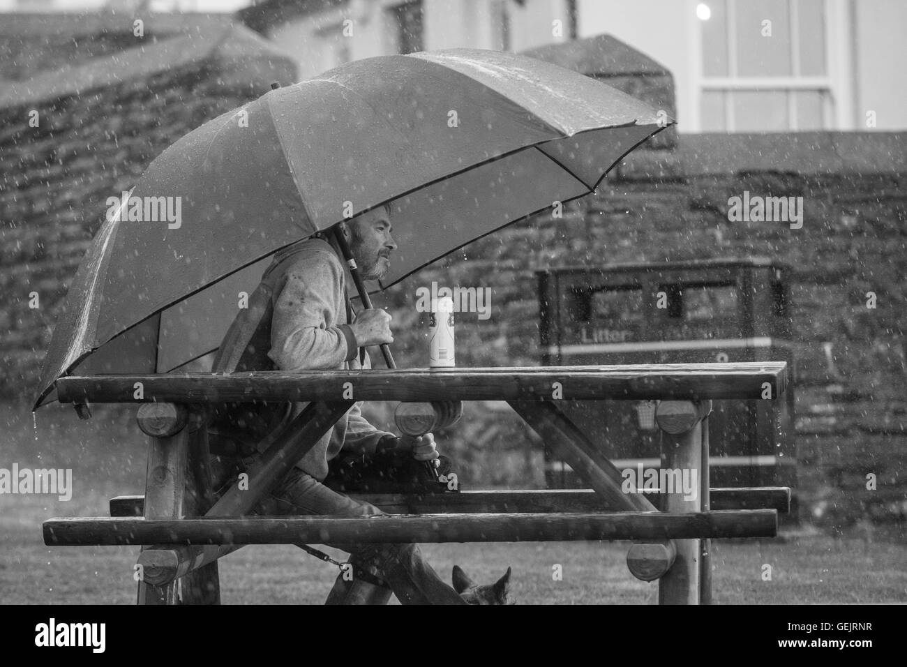 Hombre sentado en un banco bajo una sombrilla grande mientras está lloviendo fuertemente Foto de stock