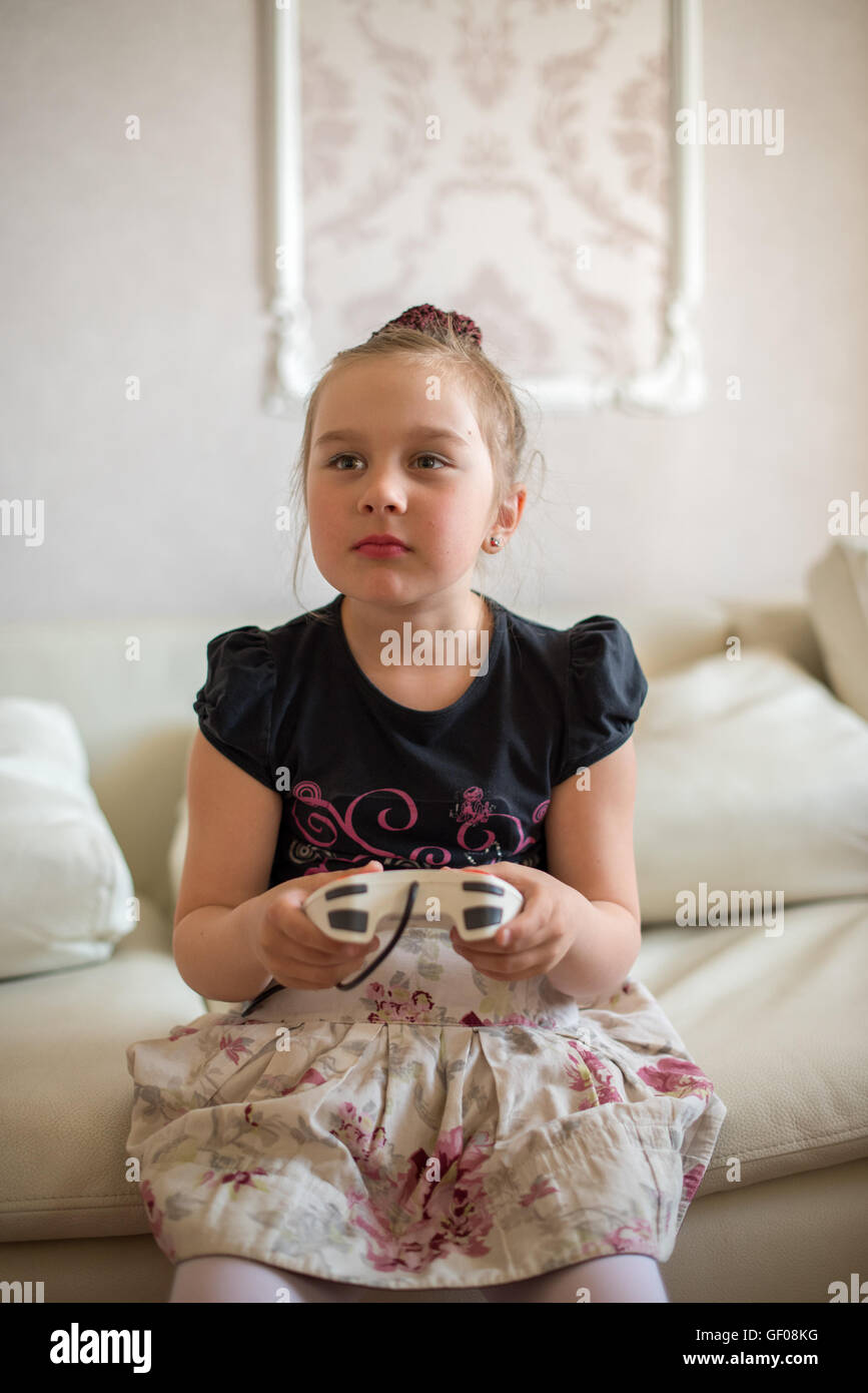 Cute Little Girl sentado en el sofá y jugar con videojuegos. Foto de stock