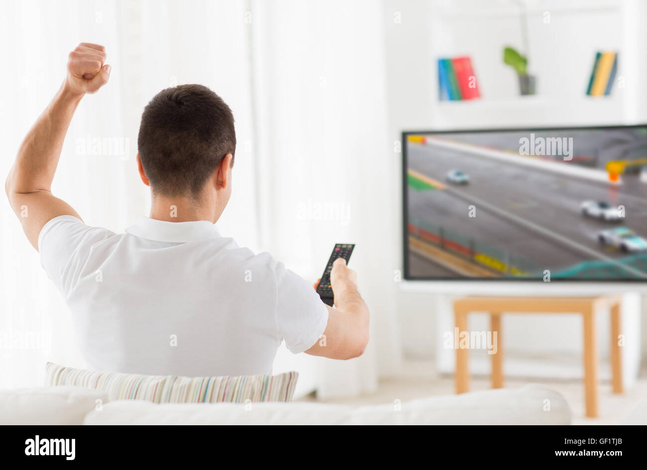 Hombre con control remoto viendo motorsports en la televisión en casa Foto de stock